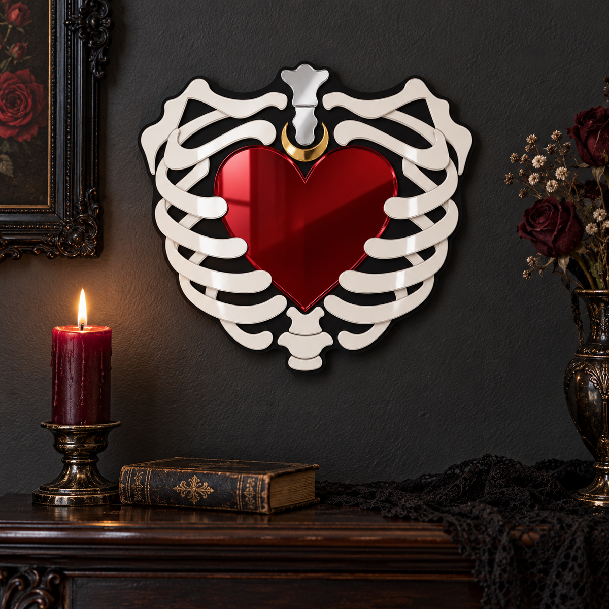 A decorative wall mirror shaped like a white rib cage around a glossy red heart, mounted on a dark wall above a wooden console table with a lit candle, book, and dried flowers.