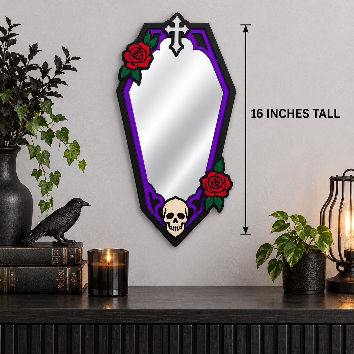 A coffin-shaped wall mirror with a black frame, purple decorative border, red roses, and a skull at the bottom, shown hanging on a light gray wall above a dark shelf with decor items. Text on the right reads '16 INCHES TALL'.