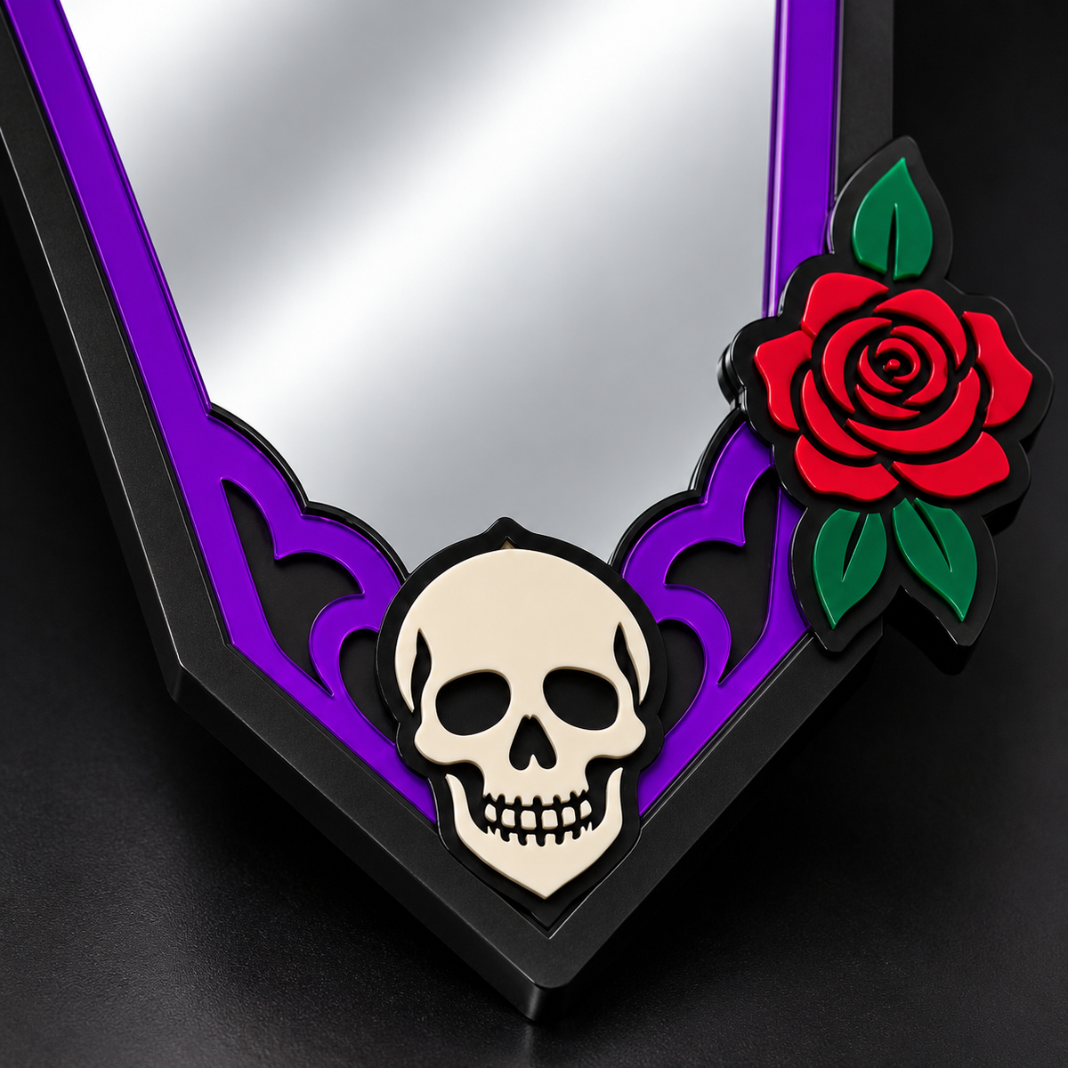 A close-up of a decorative mirror with a black frame, purple ornamental corner accents, a cream skull emblem, and a red rose with green leaves on a dark background.