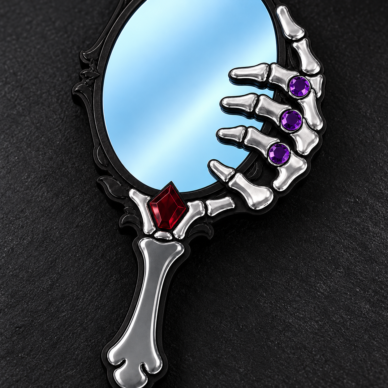 A gothic skeleton hand mirror with a silver-finished bone handle and fingers, featuring purple and red gemstone accents, set against a dark textured background.