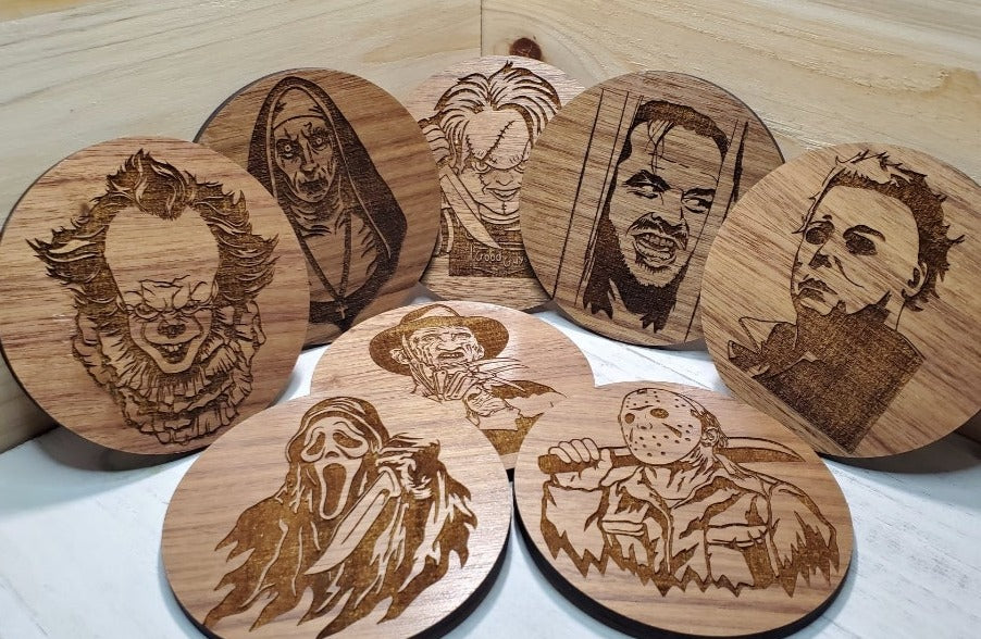 A set of four round walnut wood coasters, each engraved with a different horror movie character, displayed on a white surface.
